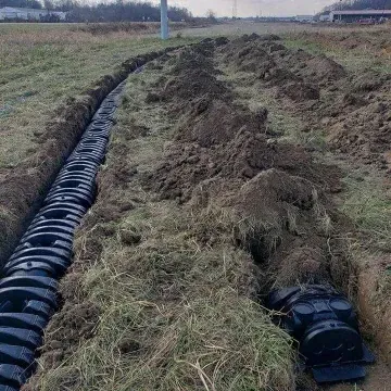 Trench filled with black plastic drainage pipes, partially buried in dirt and grass, in a field.