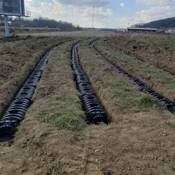Black drainage pipes in parallel trenches dug in a grassy field.