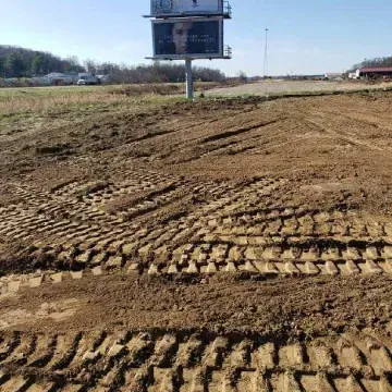 Muddy field with deep tire tracks under a billboard.