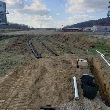 Construction site with black pipes laid in trenches, boxes, and white pipes.