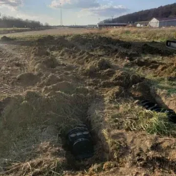 Open trench in a field with buried pipe sections; construction site.