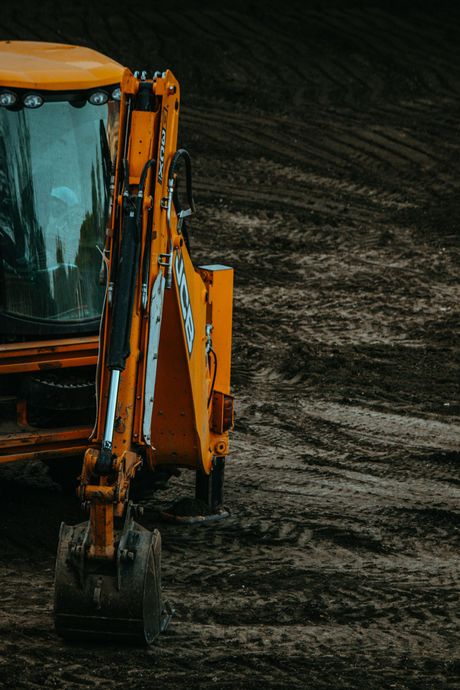 Yellow backhoe on a muddy construction site, partially visible.