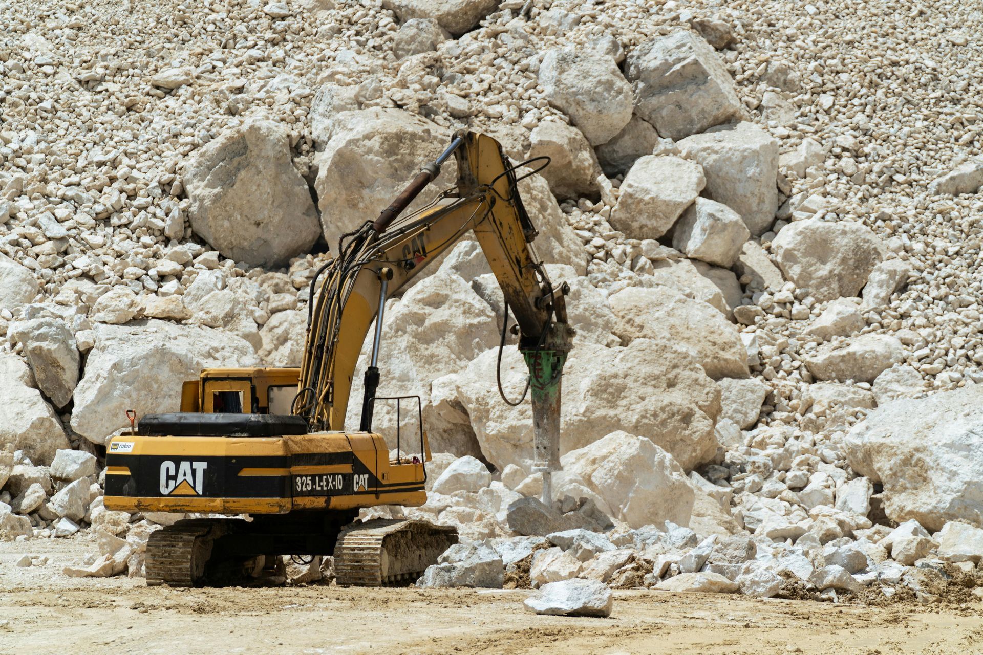 Yellow Caterpillar excavator breaking rocks in a quarry.