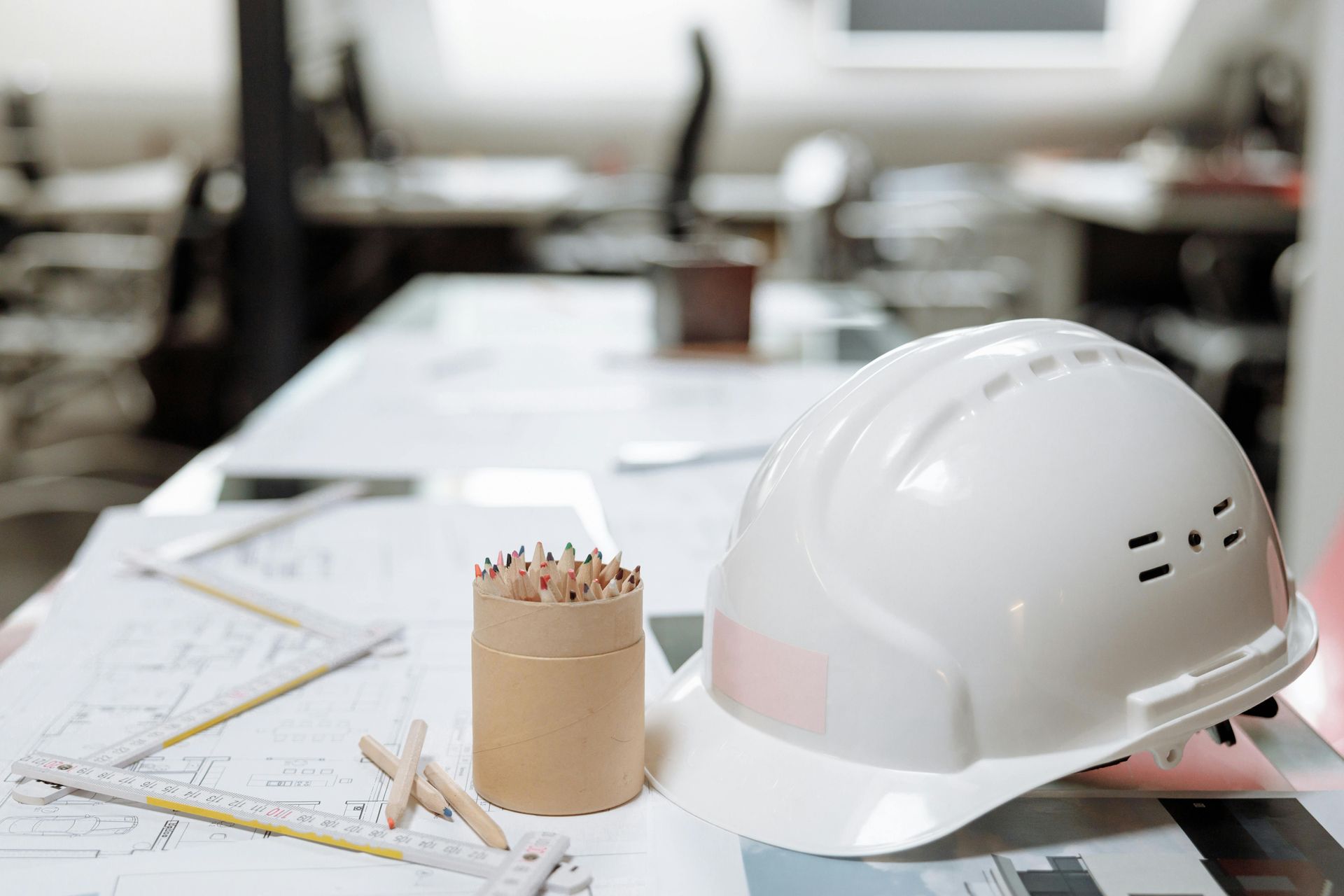 White hard hat on blueprints with pencils in a holder, in an office.