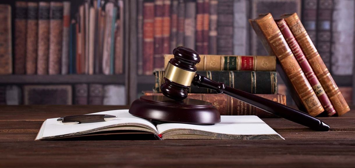 A wooden judge 's gavel is sitting on top of an open book on a wooden table.