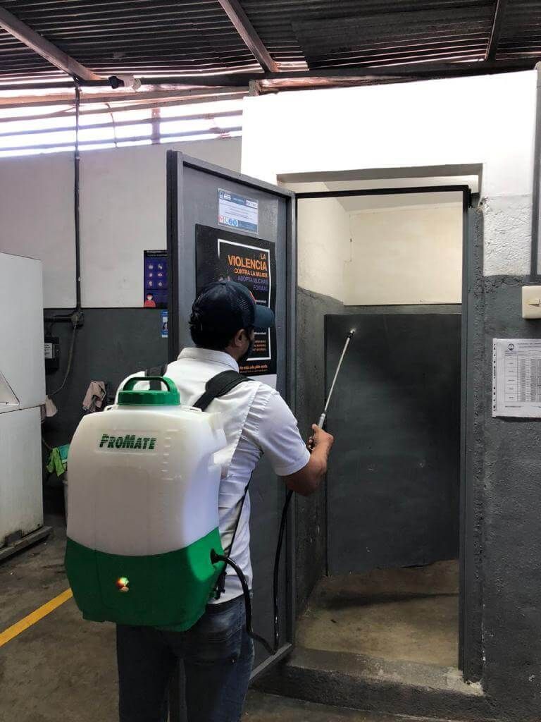 Una persona que lleva una mochila pulverizadora desinfecta el marco de la puerta 