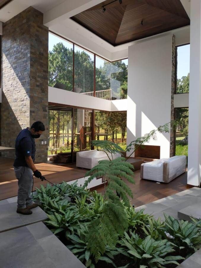 Un trabajador rocía con insecticida las plantas en el patio de una casa moderna de techos altos