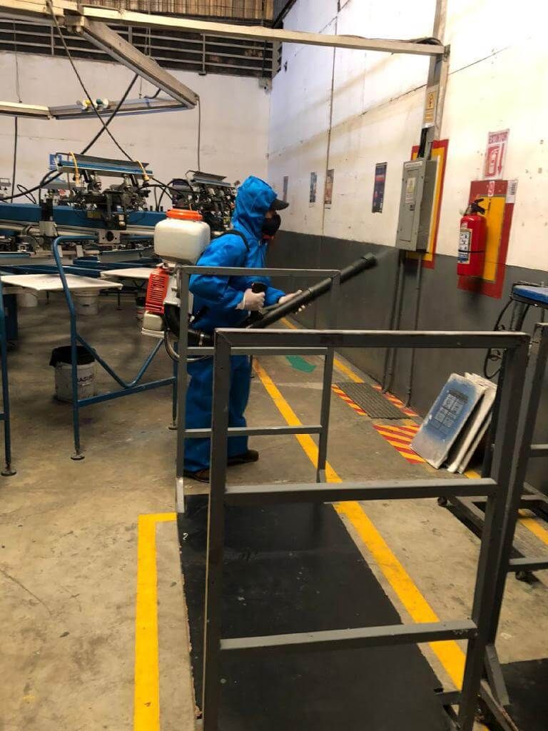 Una persona con un traje protector azul y una mascarilla utiliza un pulverizador desinfectante 