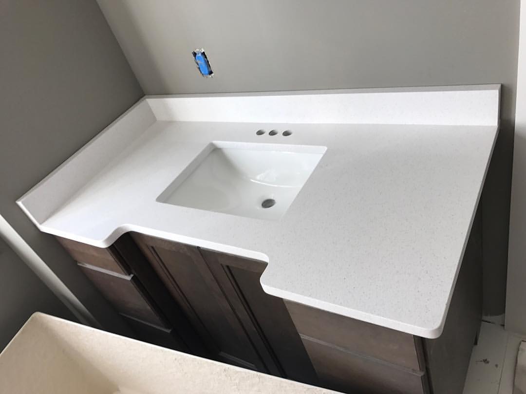 A bathroom vanity with a white counter top and a white sink