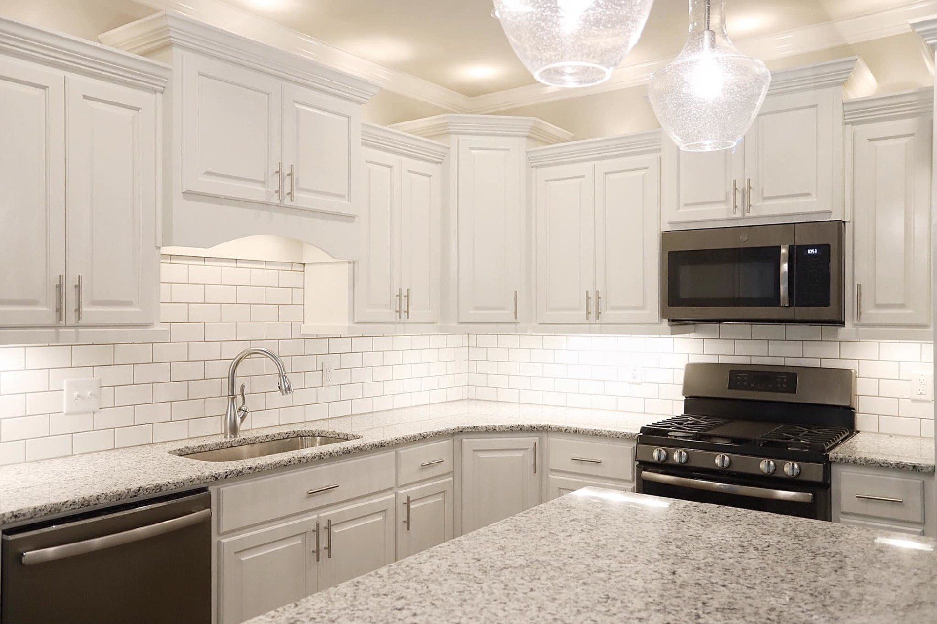 A kitchen with white cabinets , granite counter tops , stainless steel appliances and a stove.