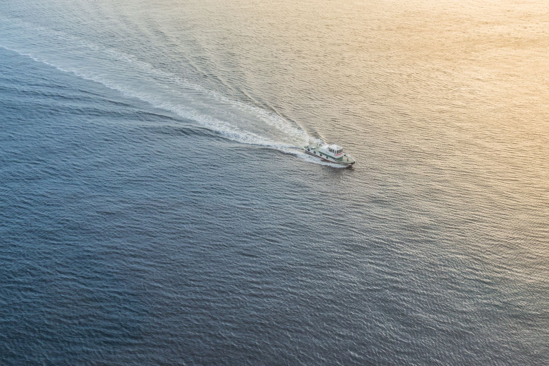 Boat travels across water, creating a wake. Blue water fades to golden light.