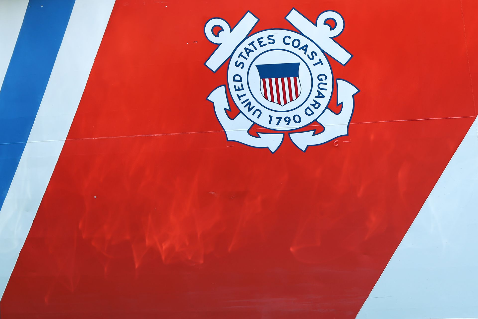 Coast Guard emblem on orange and white ship's hull with blue stripe.