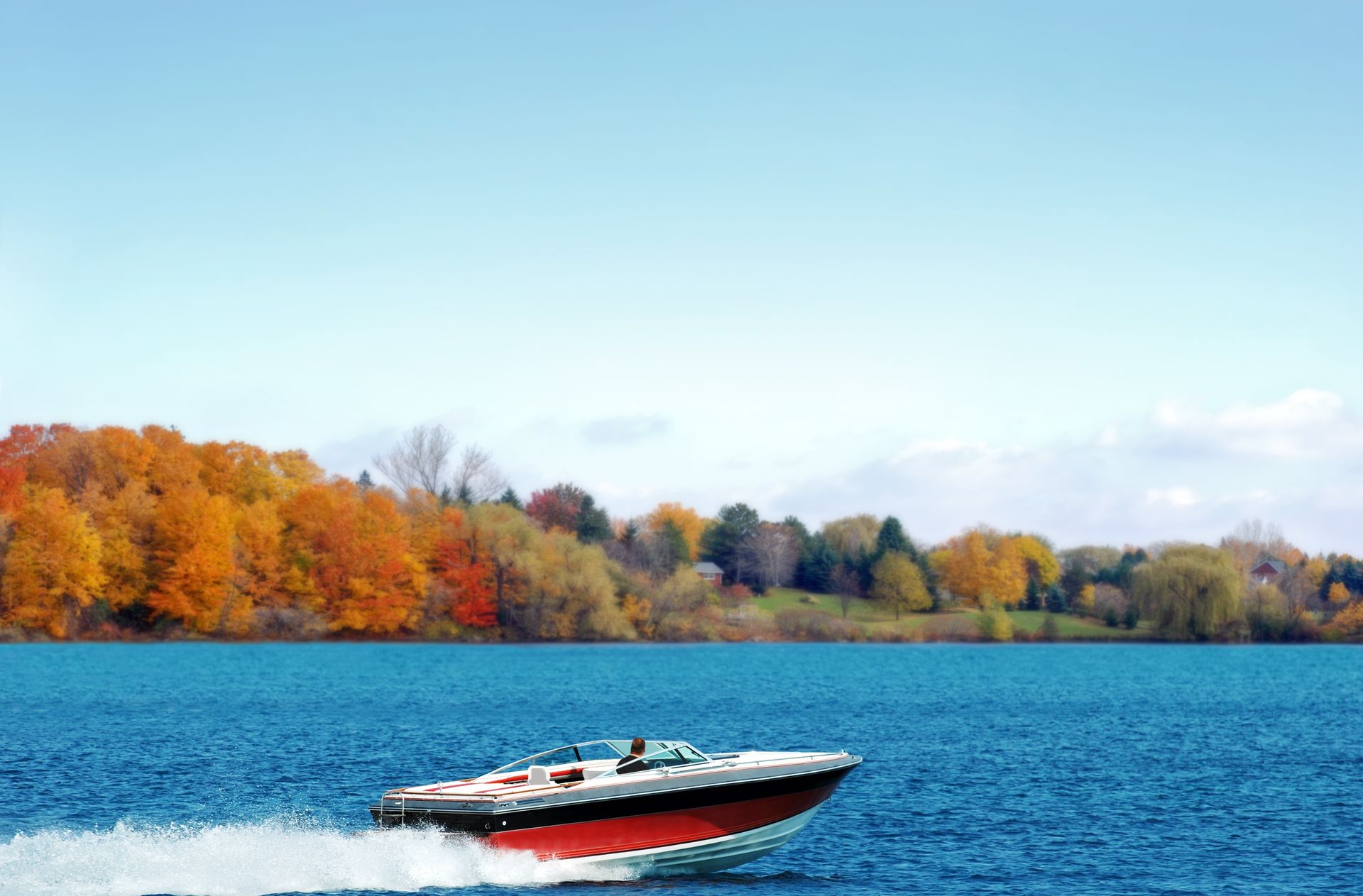 Speedboat on blue water with autumn trees in the background.