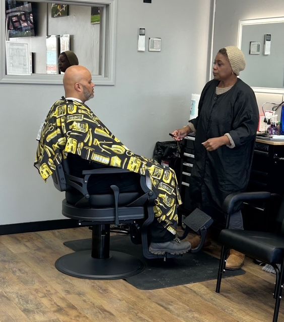 Man in barber chair, hair stylist talking, salon setting.