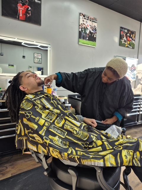 Barber giving a shave to a customer in a barber shop, using a small bottle and brush.