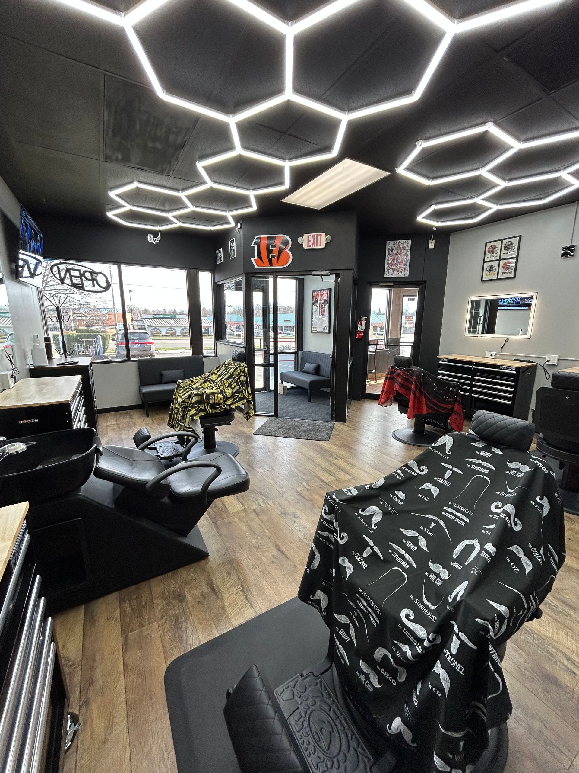 Modern barbershop interior with black chairs, hexagon lights, and large windows.