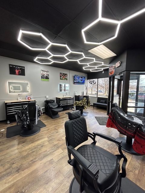Barber shop interior with hexagonal lights, black chairs, and wood-look flooring.