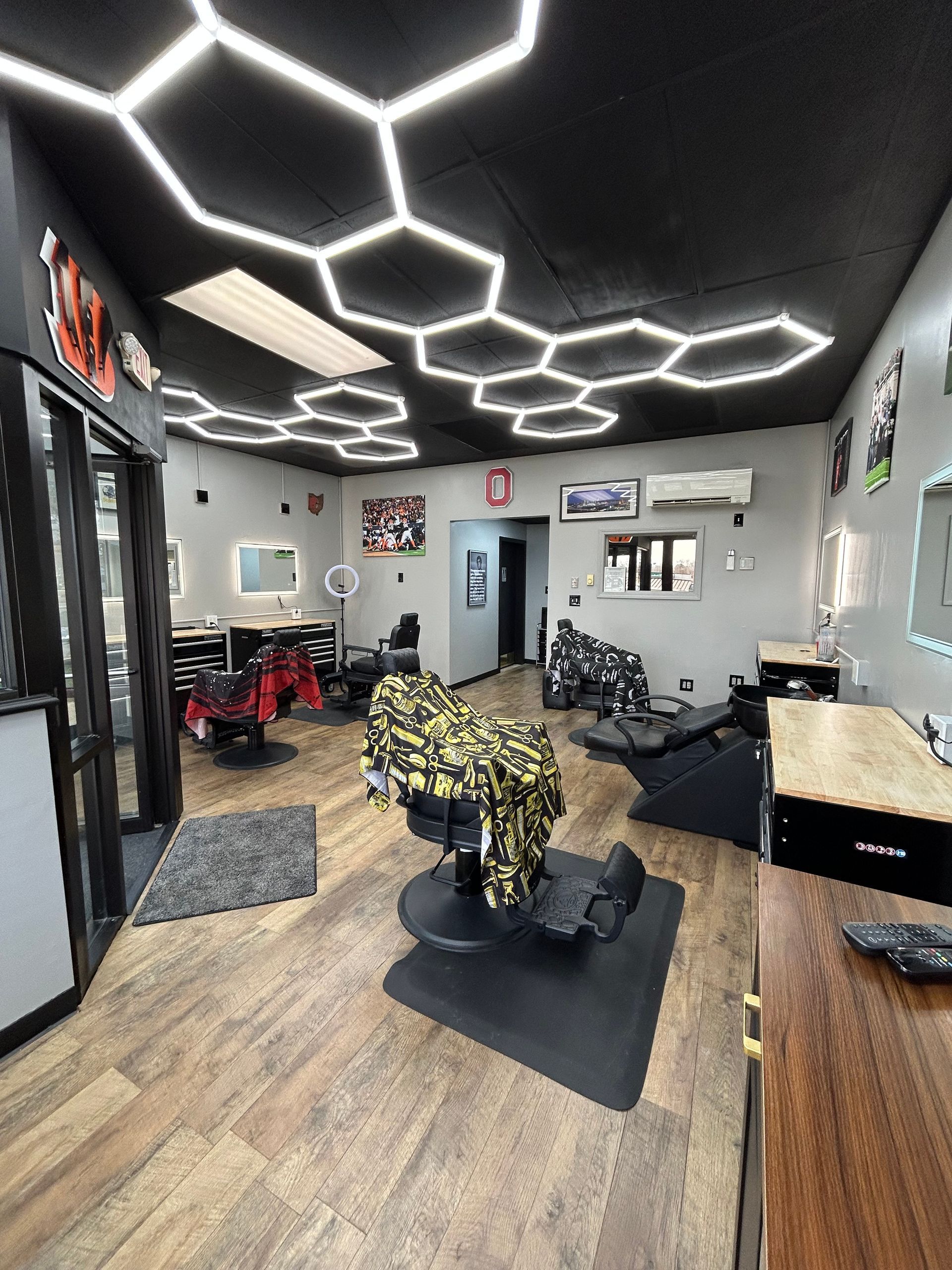 Interior of a barbershop with hexagonal ceiling lights, black chairs, mirrors, and wooden floors.