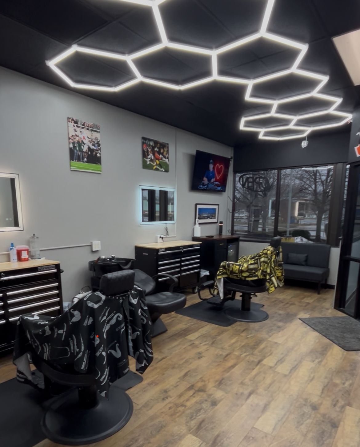 Barbershop interior with hexagon-shaped ceiling lights, barber chairs, and a TV playing.