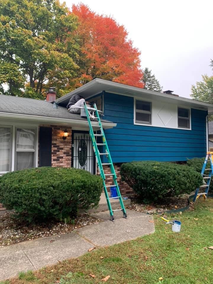A man on a ladder is painting a blue house.