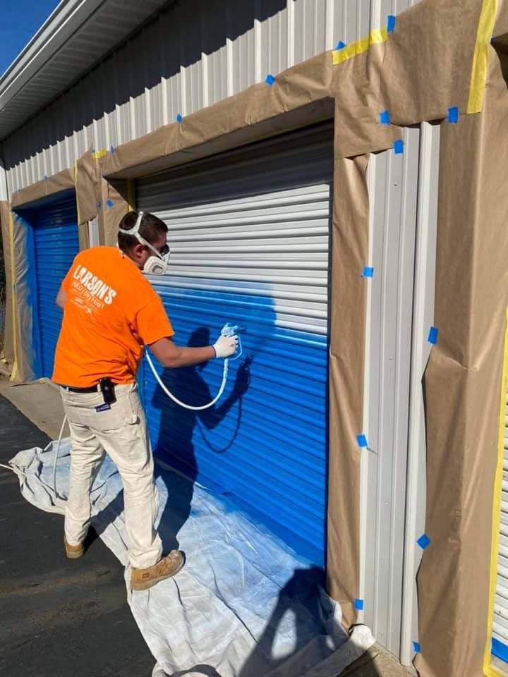 A man is spray painting a blue garage door.