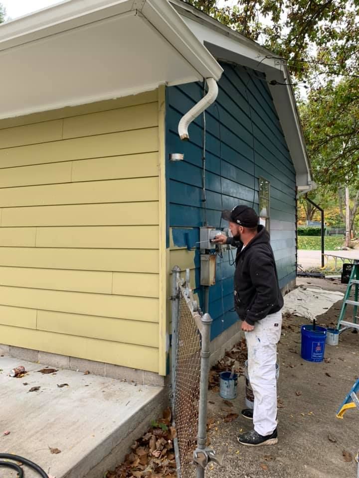 A man is painting the side of a house blue and yellow.