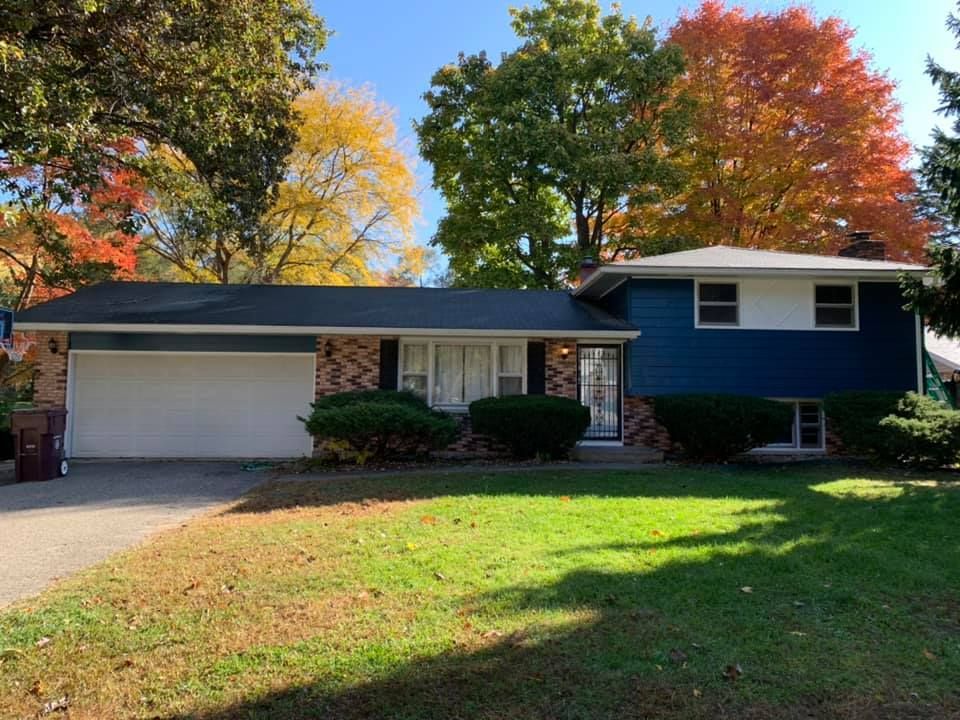 A blue house with a white garage door is surrounded by trees and grass.
