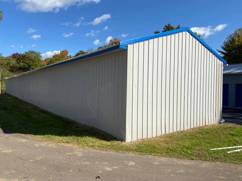 A long white building with a blue roof is sitting next to a road.