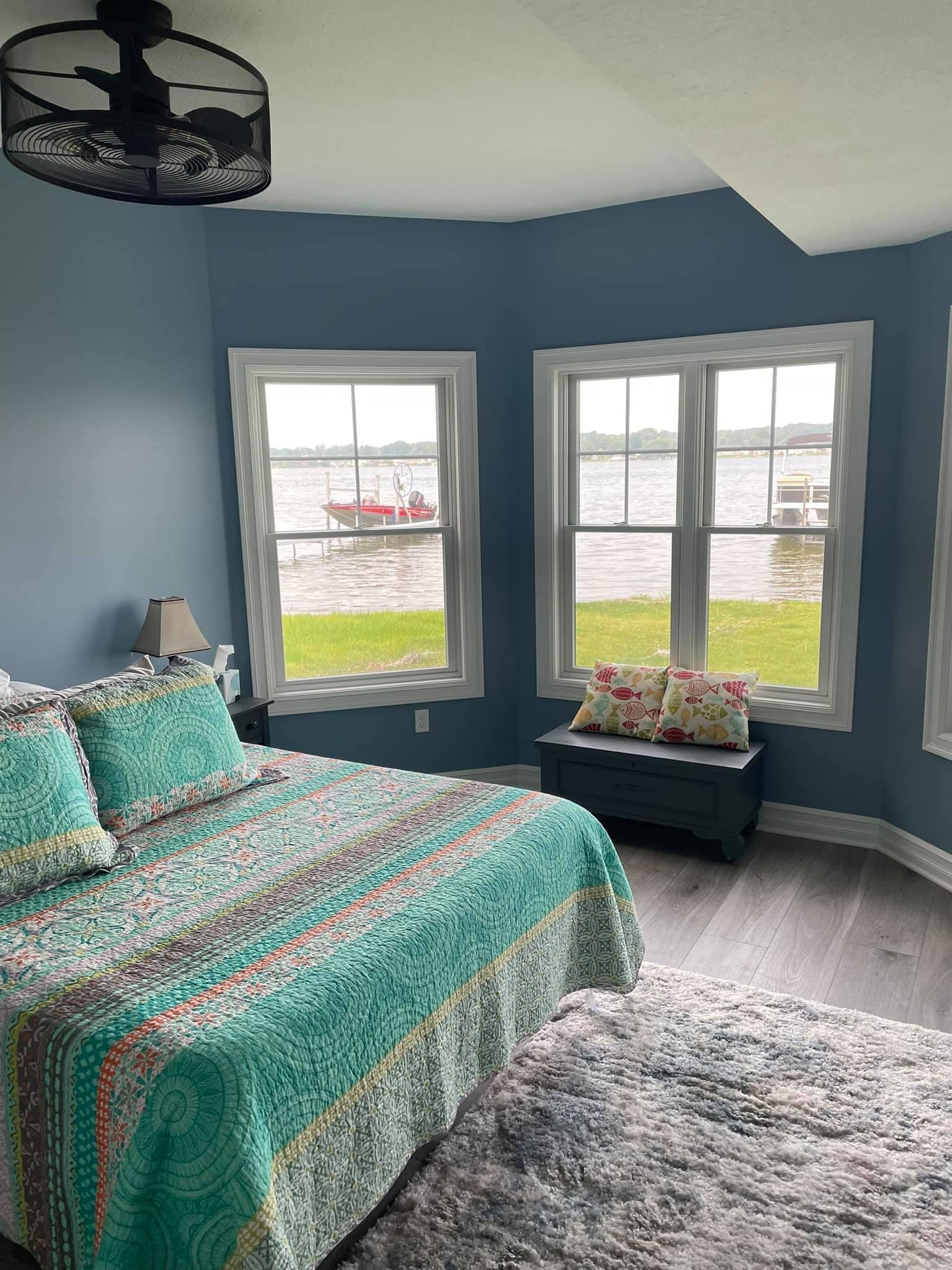 There is a large bed in the middle of the room with a view of the water.
