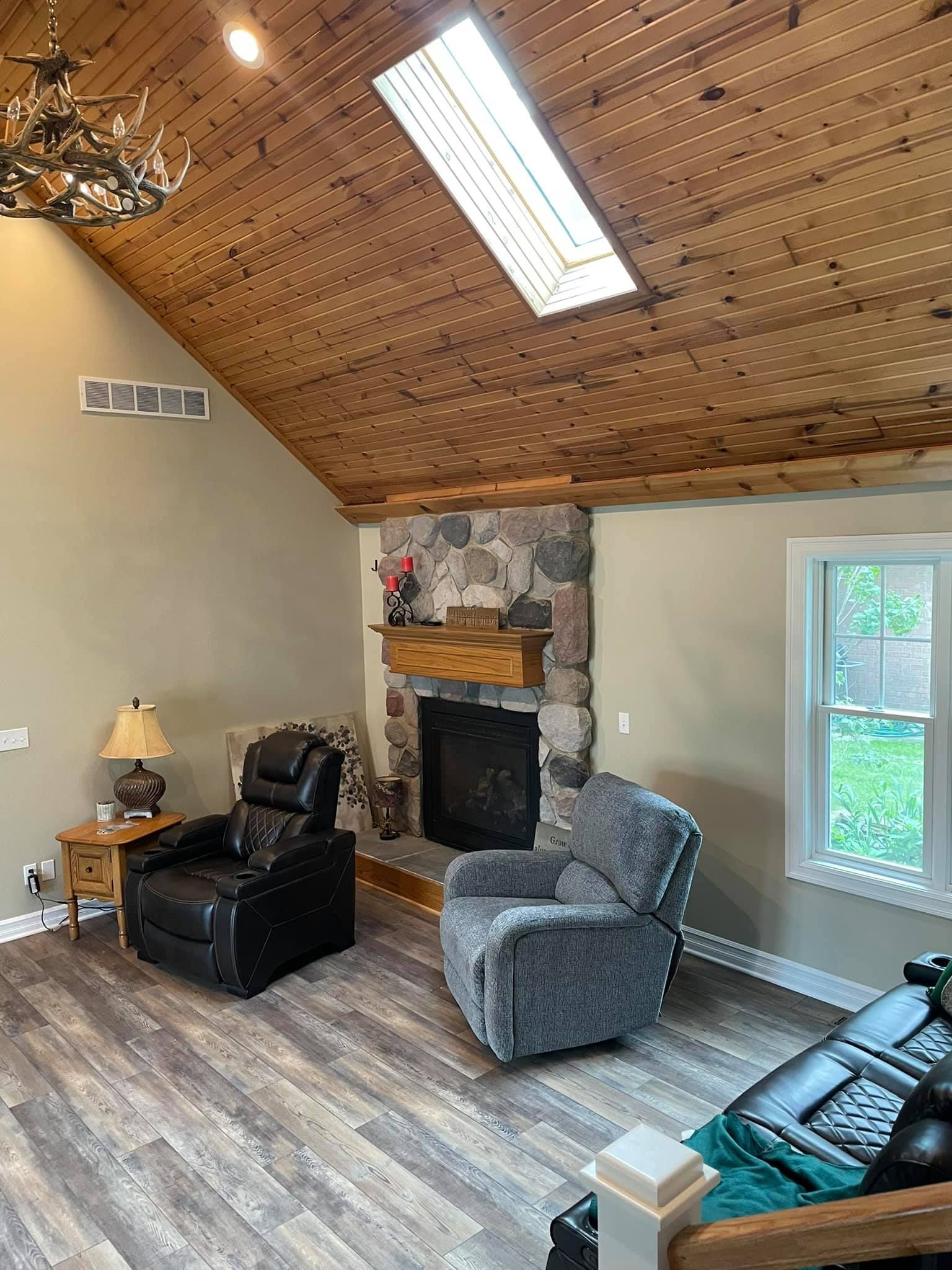 A living room with two chairs , a couch , a fireplace and a skylight.