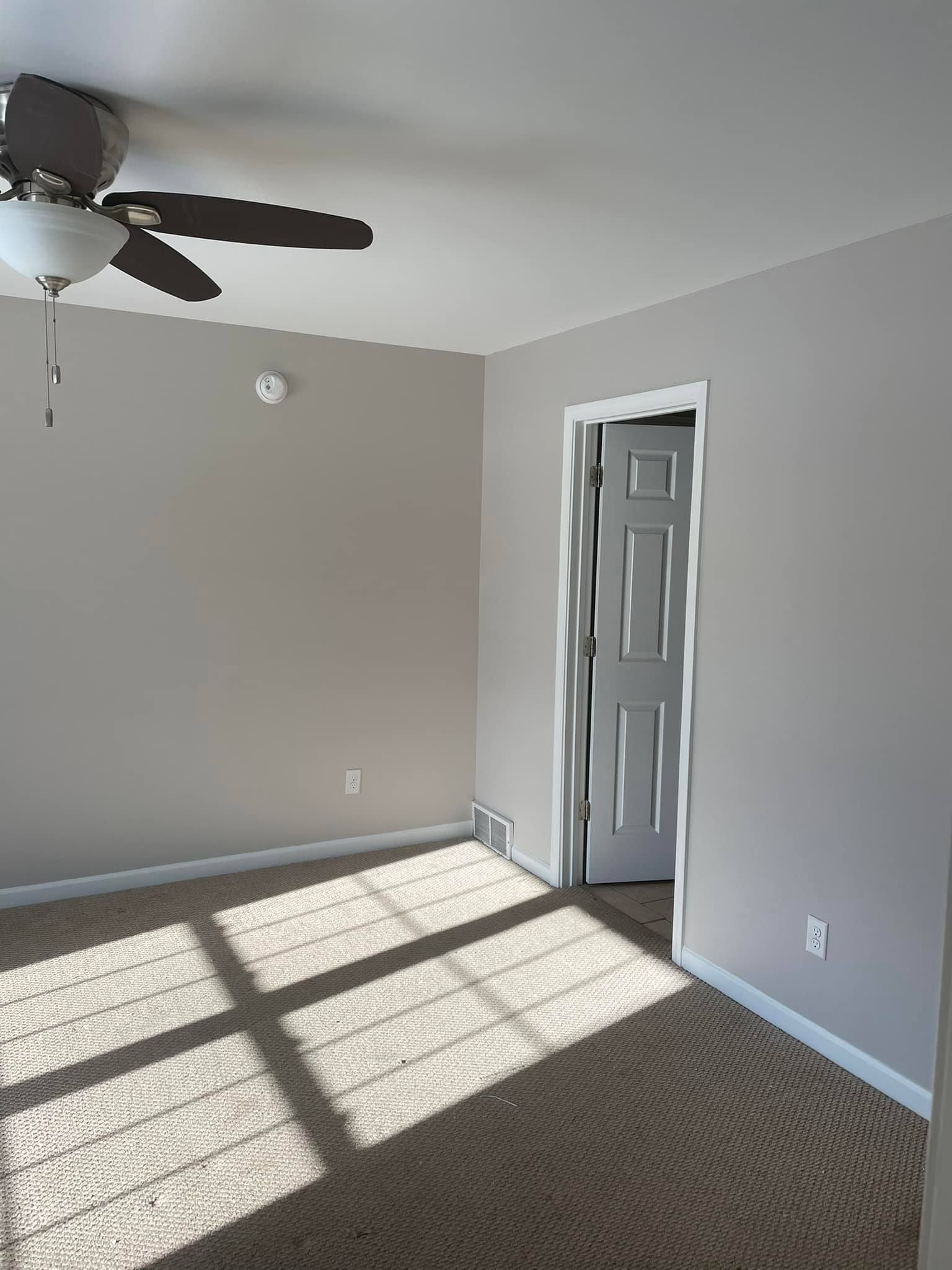 An empty room with a ceiling fan and a door.