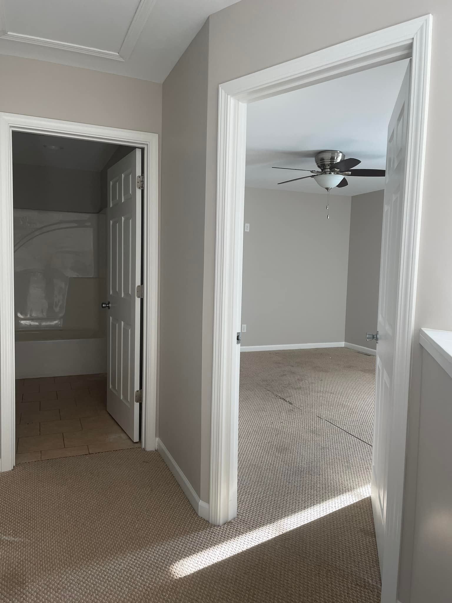 A hallway leading to a bedroom with a ceiling fan.