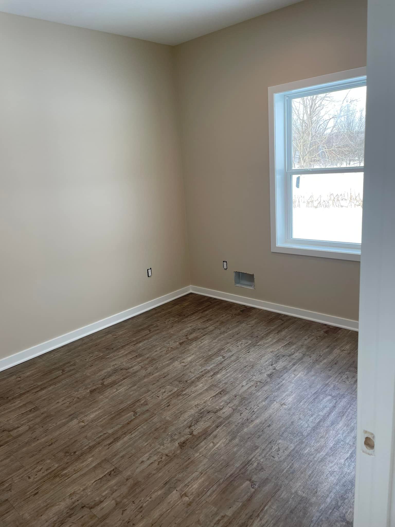 An empty room with hardwood floors and a window.