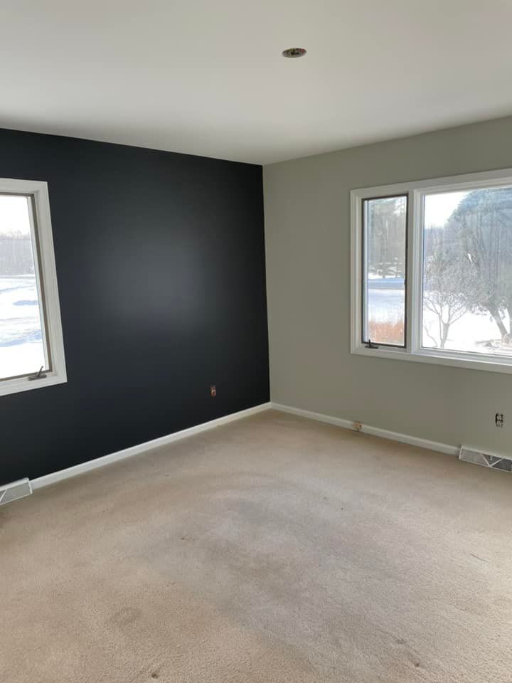 An empty room with two windows and a black wall.