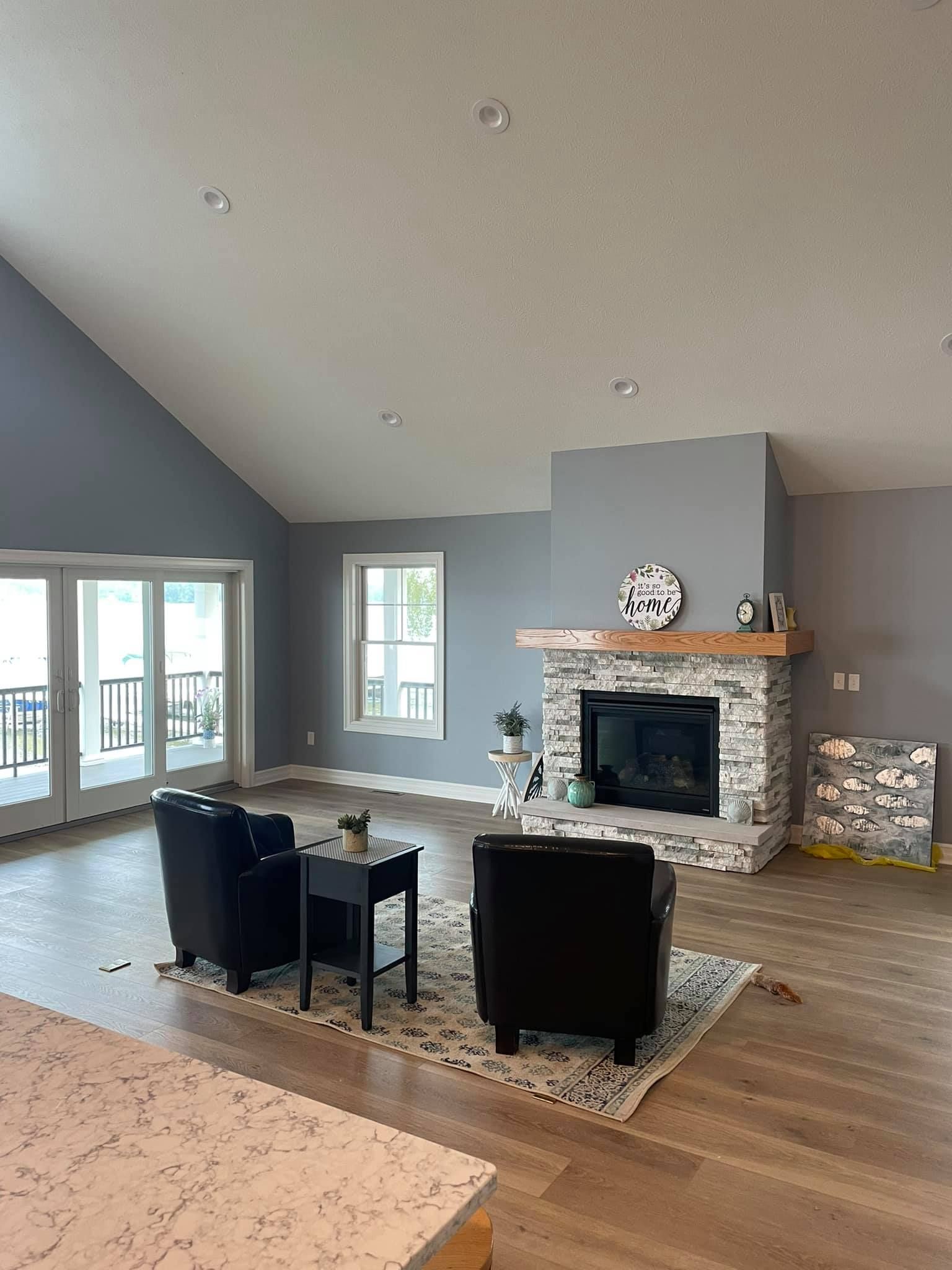 Spacious living room with gray walls, fireplace, two black armchairs, and large windows.