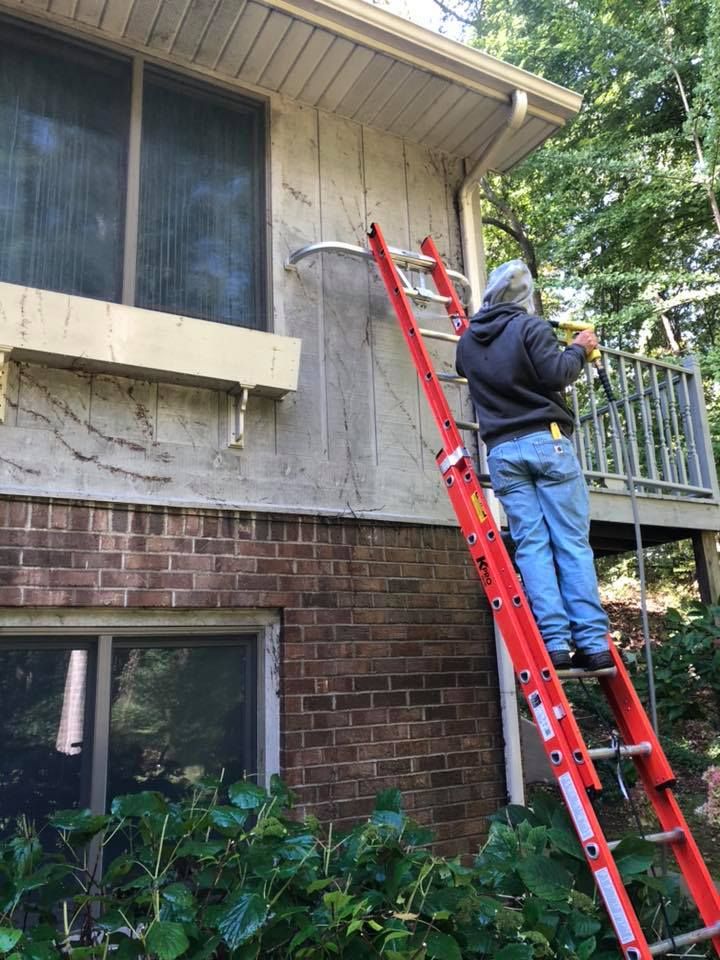 A man is standing on a ladder on the side of a house.