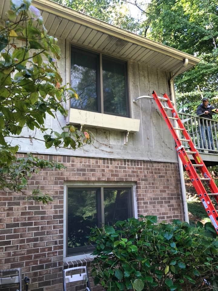 A man is standing on a deck next to a ladder on the side of a brick house.