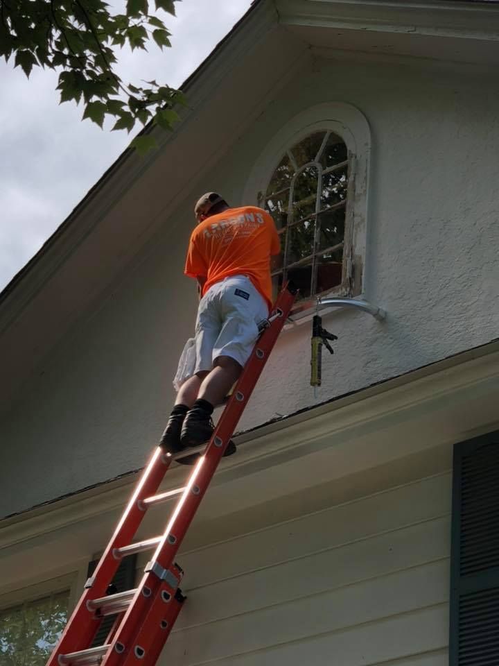 A man is standing on a ladder painting a window