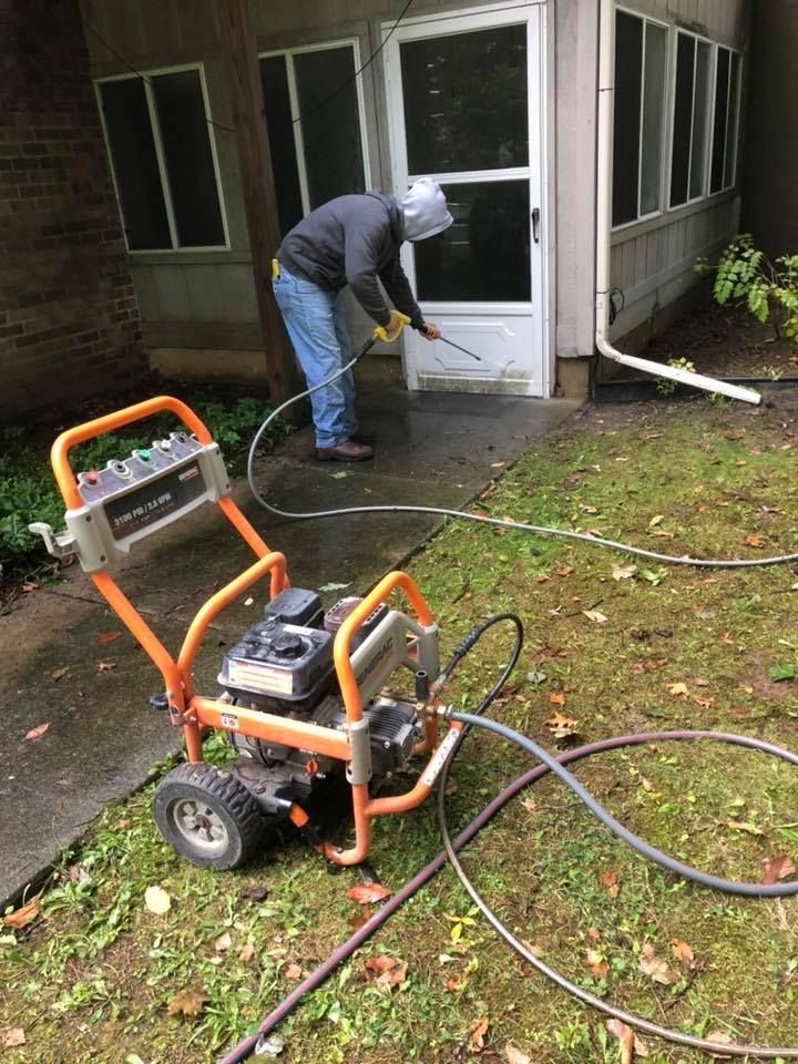 A man is using a pressure washer to clean the sidewalk in front of a house.