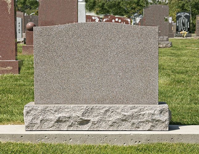 Blank gray granite tombstone in a cemetery, sitting on a base and a concrete slab.