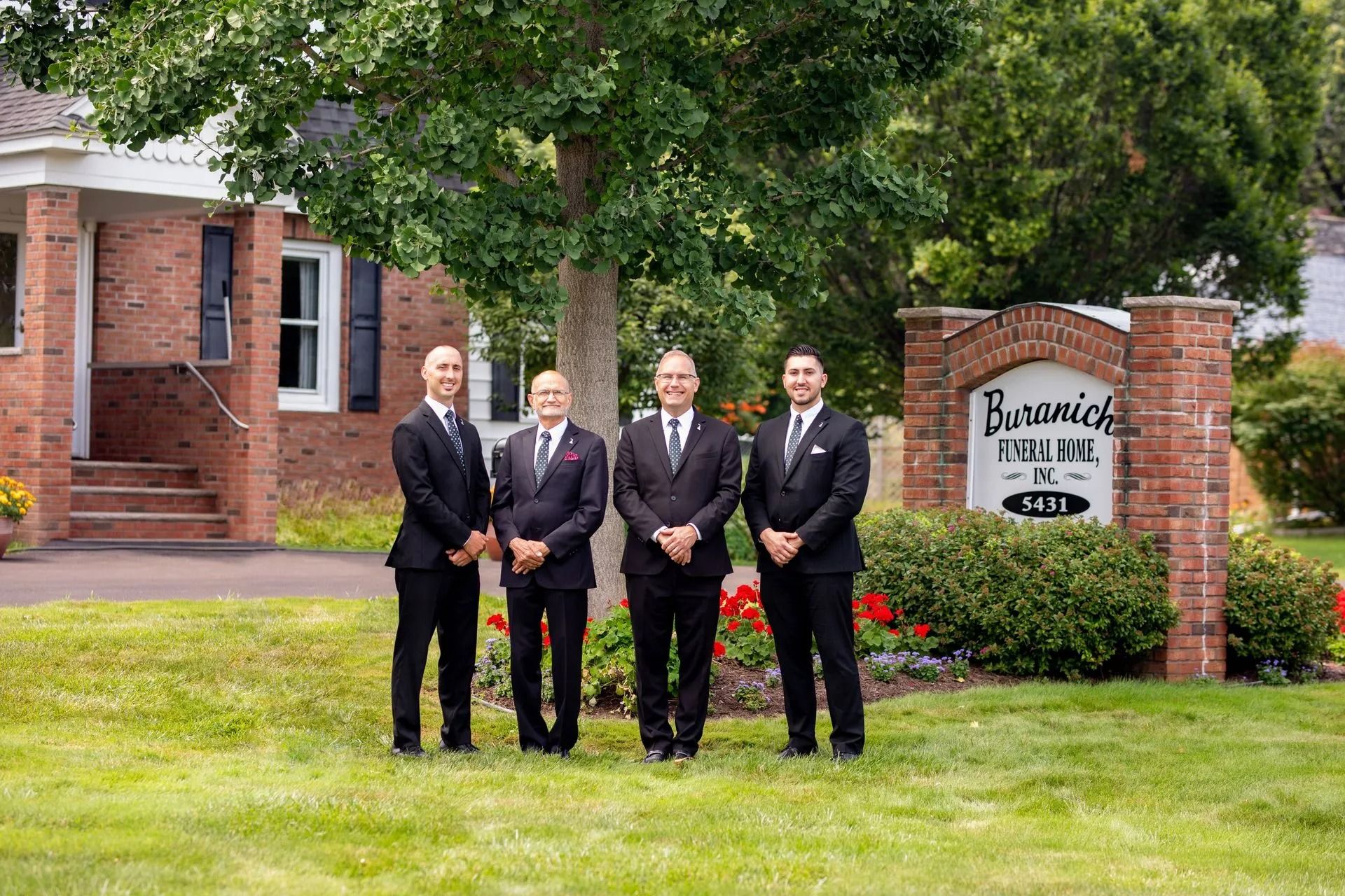 Four men in suits stand outside a brick building with a sign that reads 