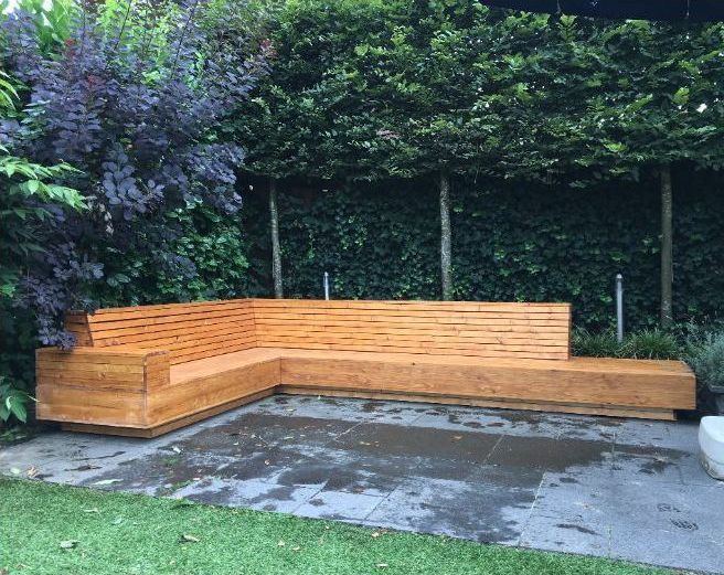 Midden in een tuin staat een handgemaakt houten bankje.