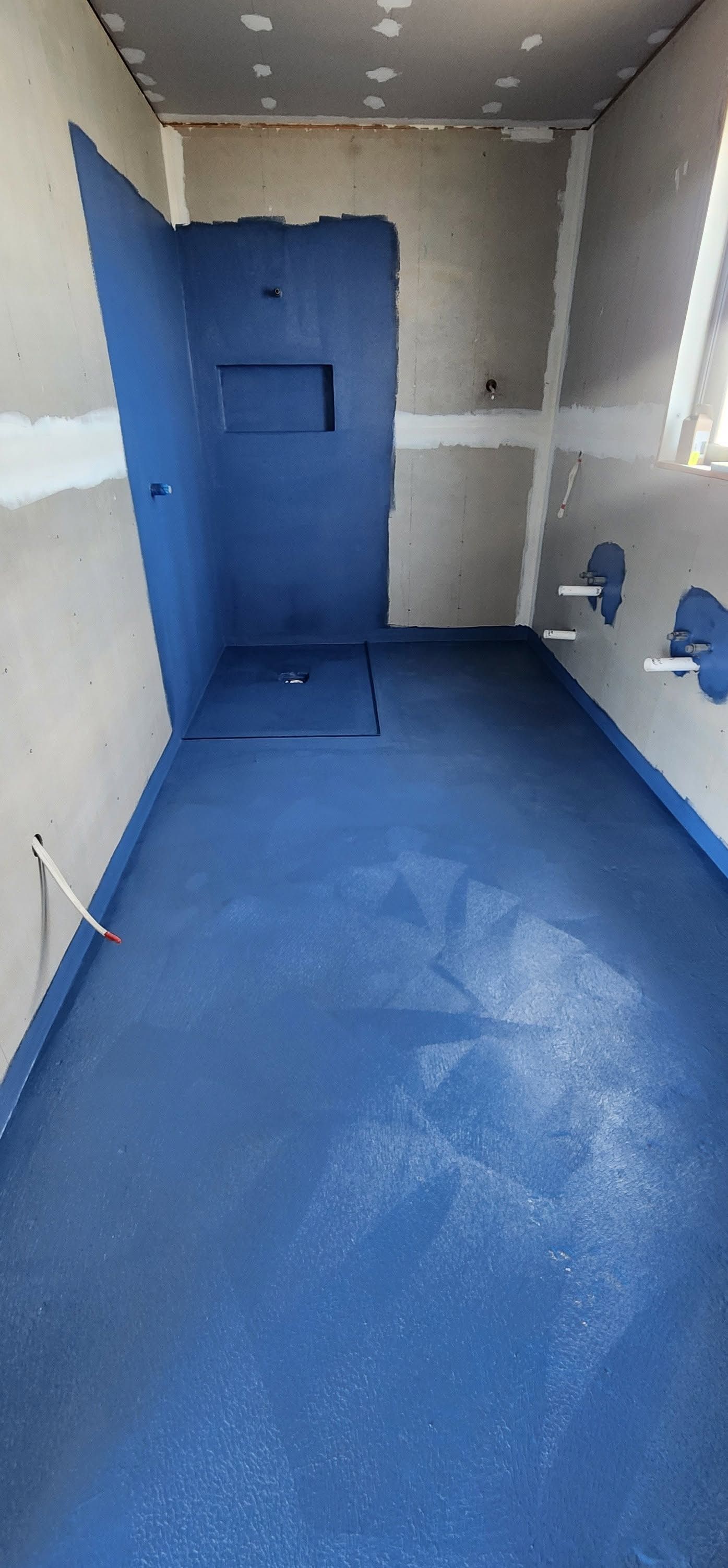 Empty tiled room under construction with gray walls and floor, unfinished plumbing visible