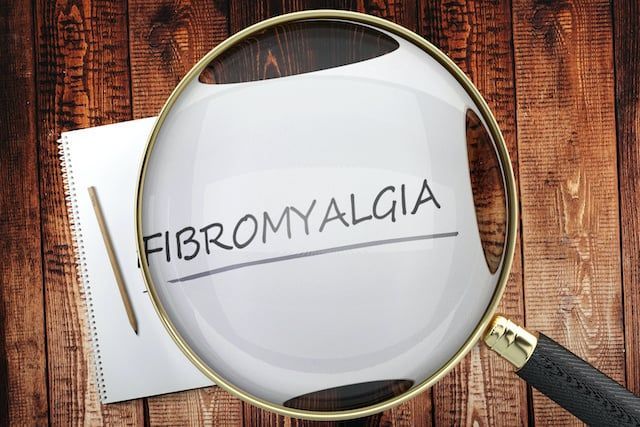 A magnifying glass is looking at a piece of paper that says fibromyalgia