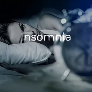 A woman is laying in bed looking at an alarm clock