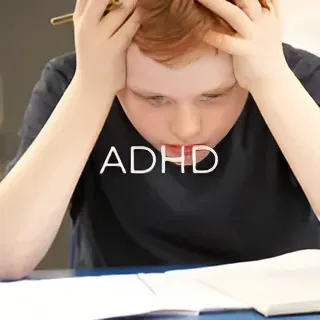 A young boy is sitting at a desk with his hands on his head