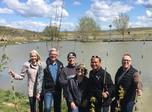 A group of people standing next to a lake holding fishing rods.