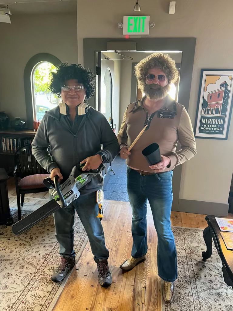 Two men in costumes are standing next to each other in a room holding chainsaws.