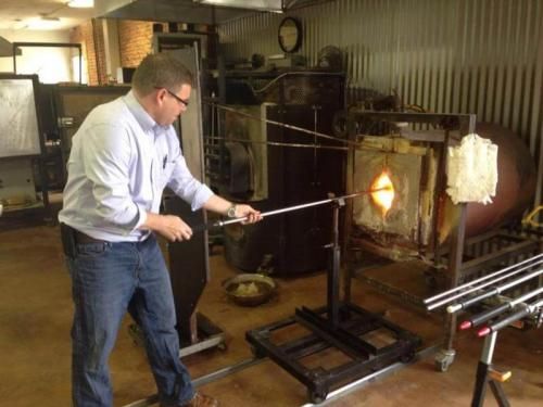 A man is working on a glass blowing machine in a workshop.
