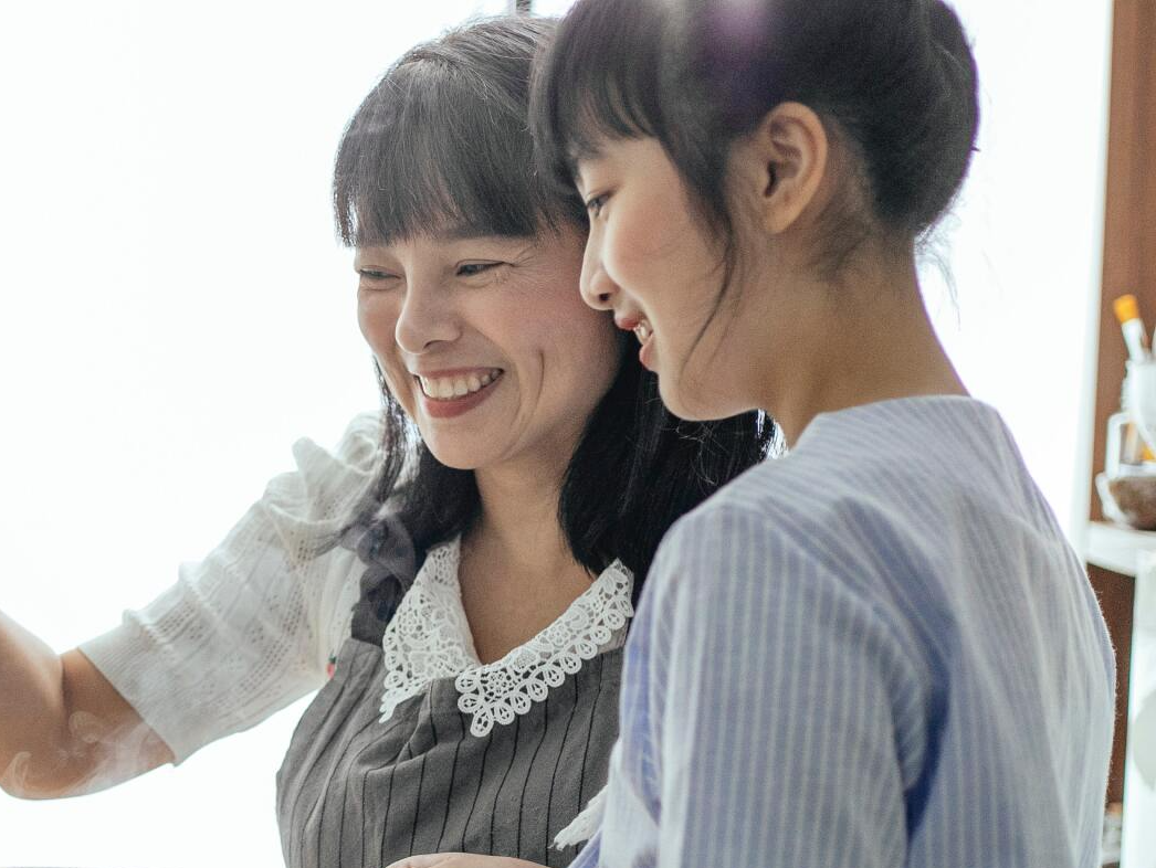 Two women are standing next to each other in a kitchen and smiling.